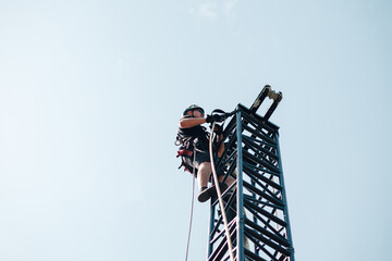 Worker in safety harness and helmet climbing a metal structure, performing installation or...