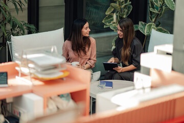Businesswomen collaborating on digital tablet in modern office terrace, discussing new project ideas