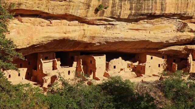 Golden sunset light bathes ancient preserved sandstone masonry structures sheltered within the giant natural alcove of Spruce Tree House