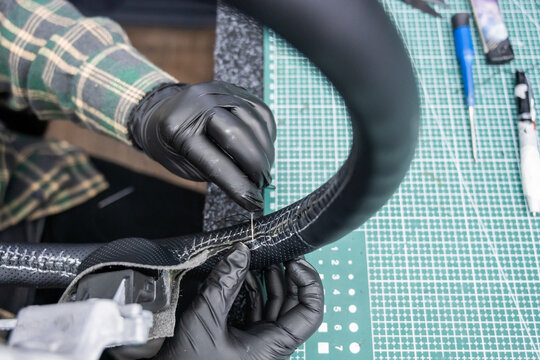 A seamstress in a workshop makes a new leather cover for a car steering wheel.