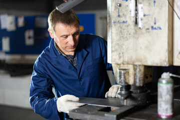 Concentrated experienced operator working on punching machine in industrial workshop, performing...