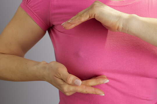 Close-up of a womans torso in a pink shirt framing her chest with her hands, illustrating breast health awareness and preventative medical education.
