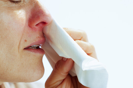 A close-up side profile of a woman wiping an irritated, red nose with a tissue, capturing the discomfort of a cold, allergy, or sinus pressure.