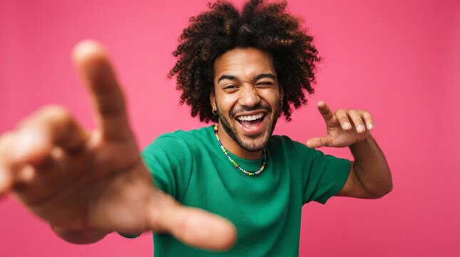 A happy African American man with curly hair and a green shirt dancing with energy on pink.