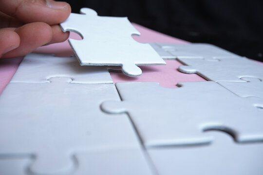 Hand pushing a puzzle piece into the gap to complete the puzzle, illustrating the concept of integration or business merger