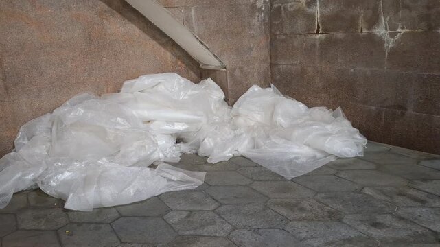 Pile of discarded plastic bubble wrap waste lying on a stone pavement outdoors. plastic pollution, recycling issue, industrial waste, packaging garbage.