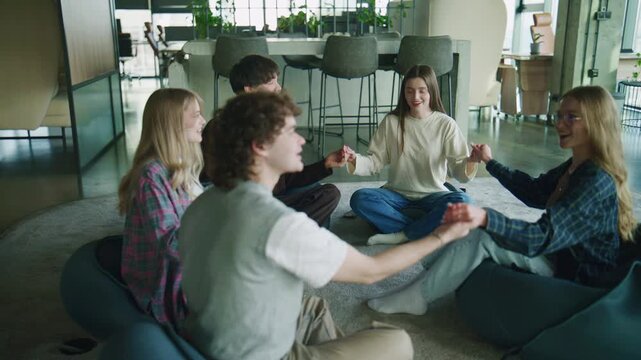 Participants hold hands and share thoughts during a psychology session in a modern building's open space. The atmosphere is focused on dialogue and connection.