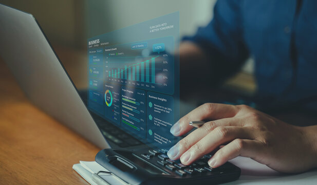 Business person working on laptop and using calculator with virtual financial display and sales insights