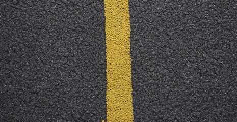 Naklejka premium Top down view of a yellow painted line on dark grey asphalt road surface with textured pavement