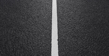 Top down view of a single white painted line dividing a textured black asphalt road surface © Nurjahan _Studio