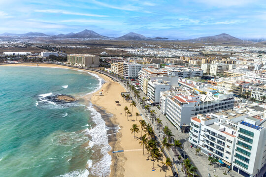 aerial of Arrecife, Lanzarote with scenic beach and palm trees and white painted houses and volcano at horizon