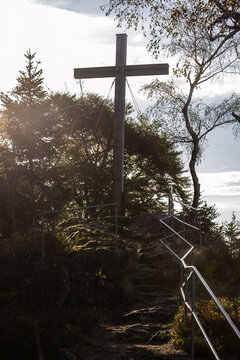 Summit cross on Mount Hennenkobel in the Bavarian Forest with rocky trail, railings and forest surroundings