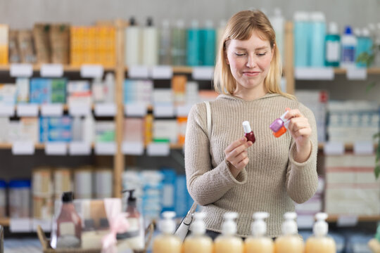 Blonde woman in jumper choosing nail polishes in a European pharmacy