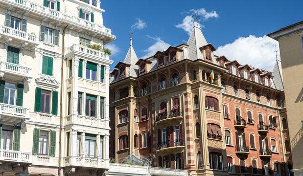 Fachadas de elegantes edificios hist&oacute;ricos europeos con balcones, postigos verdes y detalles arquitect&oacute;nicos bajo un cielo azul soleado.