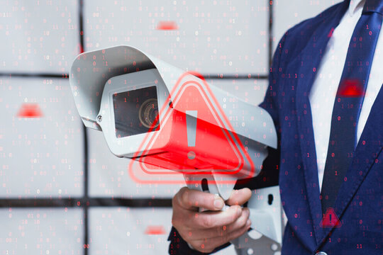 Security camera held by businessman in suit with red warning sign overlay and binary code. Cybersecurity breach, cctv surveillance system hack, data privacy risk and network protection concept.