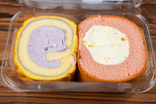 Two flavored swiss roll cake slices placed inside clear plastic takeout box