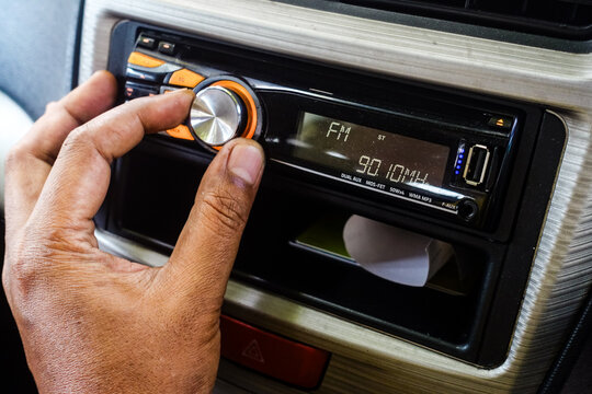 Close-up of a person's hand turning the volume knob of a car head unit stereo player, tuning the FM radio station inside a vehicle dashboard.