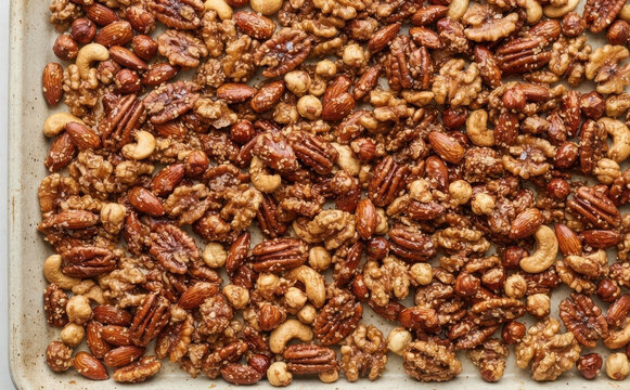 Candied mixed nuts roasted on a baking sheet, featuring glazed pecans, almonds, walnuts, and cashews for sweet holiday snacking concepts and homemade gifts