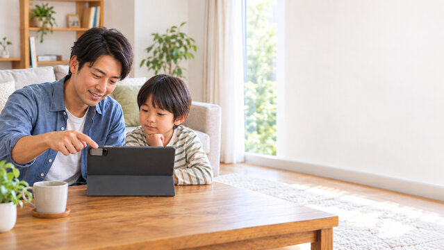 Father guiding his son as they use a tablet together at home，自宅で息子にタブレットの使い方を教える父親