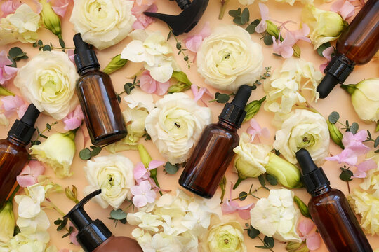 Cosmetic serum bottles on delicate flowers background, natural scincare cosmetics, beauty and facial care concept image, selective focus, shallow DOF