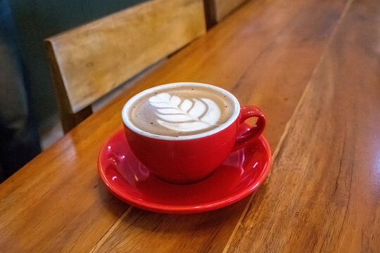 Fresh Cappuccino with Rosetta Latte Art in Red Ceramic Cup on Wooden Cafe Table