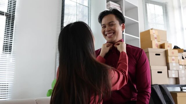 Asian couple having fun while getting dressed for work. Playful Asian woman adjusting her boyfriend's shirt collar while they are joking and laughing. Loving relationship in a work.
