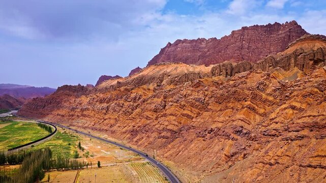 Aerial view of the winding Duku Highway passing through red sandstone mountains and arid desert landscape in Xinjiang, China
