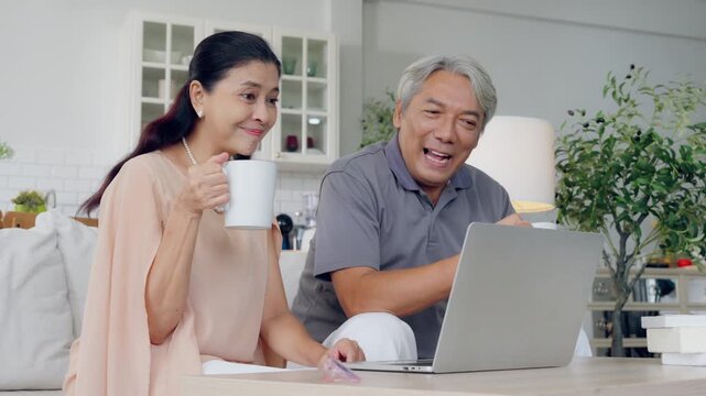 Senior spouses using laptop together sitting on couch at home. Elderly couple, hug and love on sofa with happy marriage, support and conversation of retirement home