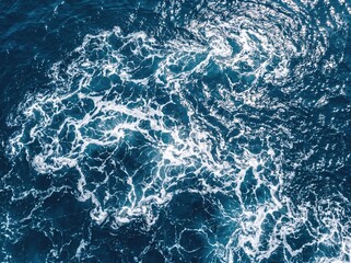 Fototapeta premium Turbulent ocean water with swirling white foam and dark blue depths.