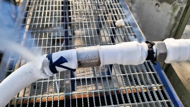 Dangerous gas leak from frozen cryogenic pipeline with thick frost and escaping vapor in industrial plant