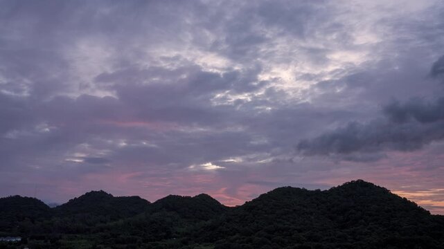 Time lapse view of a beautiful golden sunrise behind a lush green mountain range. Vibrant cloudy sky with orange and yellow morning sunlight over the forest landscape.