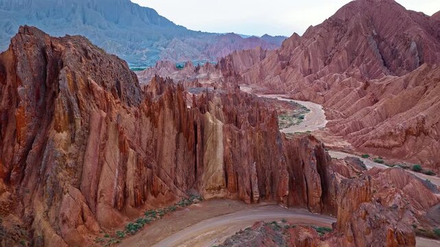 Aerial view of a winding dirt road through rugged red rock canyon ridges in the Red Mountain Stone Forest, Kuqa, Xinjiang, China