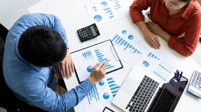 Analyzing business data Two professionals review financial reports and charts at a desk with laptops and a calculator