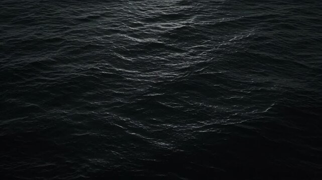 Dark sea surface with gentle wave movement, black water texture, subtle ripple patterns, moody ocean atmosphere, tranquil marine background for abstract nature footage and ocean themed design projects