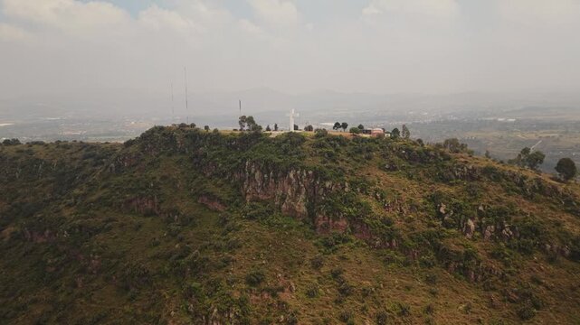 Smooth aerial drone approach to a white cross and telecommunications antennas on a lush mountain summit in Texcoco, Mexico