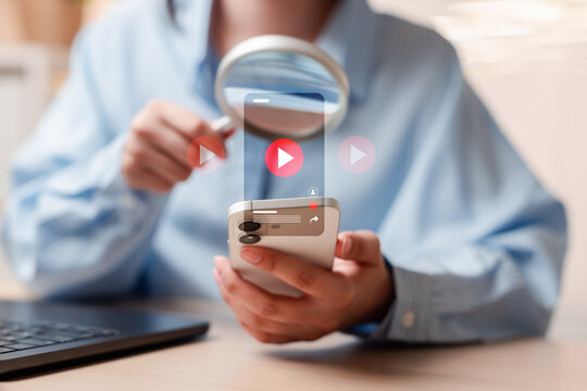 Video content search and media streaming analysis. Woman hand holding magnifying glass over smartphone finding video player.