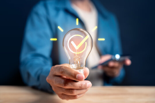 Business idea innovation solution and success approval. Woman hand holding lightbulb with check mark and smartphone.