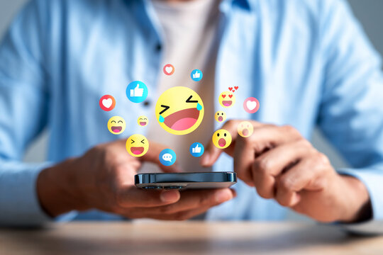 Social media network communication and online engagement reaction. Man hand holding smartphone using emoji emoticon heart like and laugh face.