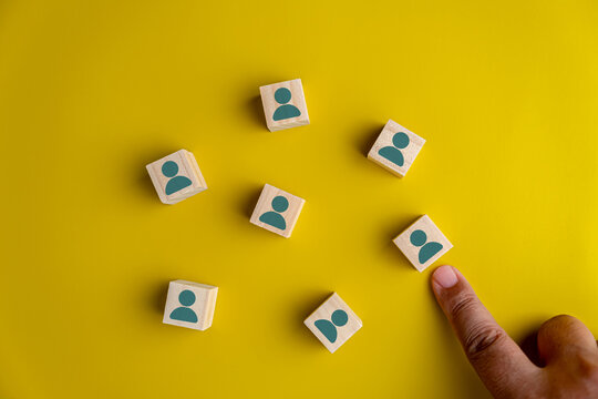 Hand choosing wooden block with person icon on yellow background for recruitment, human resources management, and candidate selection concept