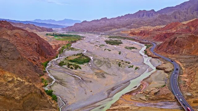 Aerial view of a braided river winding through dry desert canyons and mountain valleys along the Duku Highway in Xinjiang, China