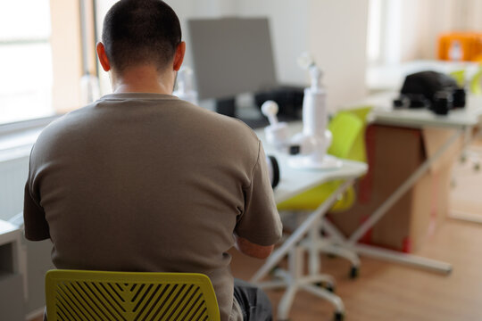 Back View Of Male Programmer Working In Modern Technology Laboratory. Tech specialist sits at his desk developing innovative software inside a laboratory