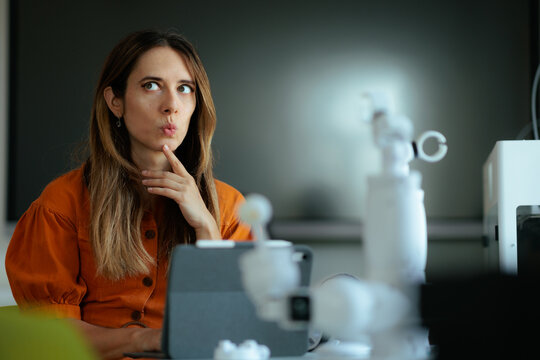 Pensive Female Educator Analyzing Complex Digital Data In Tech Laboratory. Thoughtful informatics teacher touches her chin while examining advanced classroom equipment