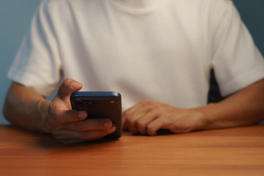 Close-up of a young man's hand using a smartphone on a wooden table. Concept of technological communication for online business, internet connectivity, chat, social media, and modern mobile networks.