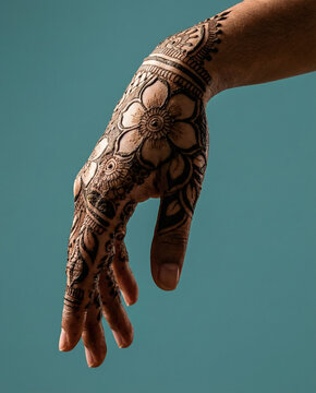 Female hand adorned with bold floral henna art posed against a solid teal background