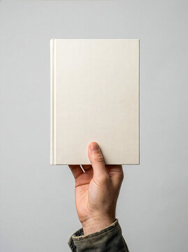 Hand holding blank hardcover book mockup on gray background