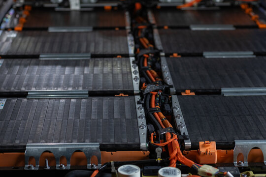 Electric vehicle battery pack with lithium-ion modules, high-voltage orange cables and metal housing in automotive workshop, EV energy storage, engineering and repair technology.