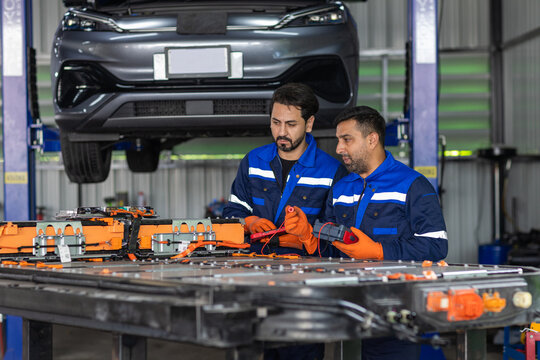 Two man engineer electric vehicle technicians testing EV battery pack with diagnostic tools in an automotive workshop, battery maintenance, electrical inspection, teamwork and engineering technology.