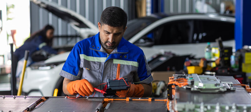 Man technician Electric vehicle testing high-voltage EV battery pack with digital multimeter in automotive workshop, electrical diagnostics, maintenance and battery service technology.