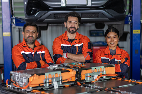 Team of electric vehicle technicians standing with EV battery pack in an automotive workshop, representing skilled workforce, battery maintenance, engineering, teamwork and clean mobility technology.
