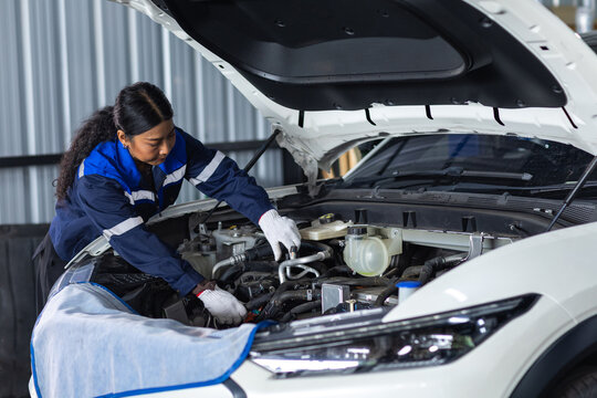 Female automotive technician inspecting vehicle under the open hood in professional workshop, car maintenance, mechanical service, skilled labor and automotive repair technology.